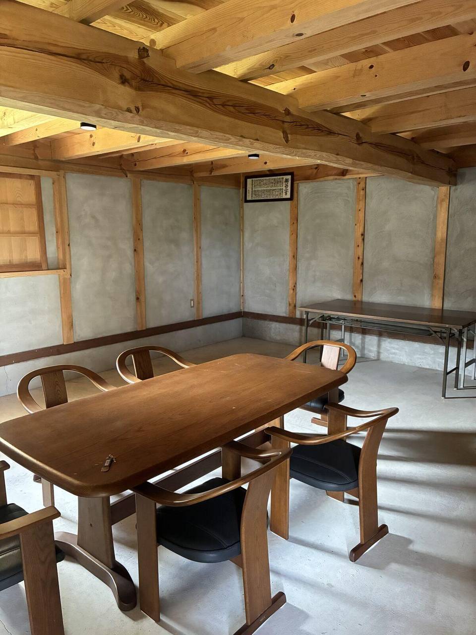 蔵の1階。太い梁がむき出しの天井の下に、木の大きな机と椅子が6脚置かれ、奥の壁ぎわに折りたたみの長机が寄せてある